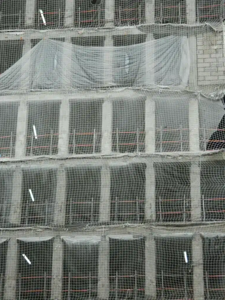 Filets de sécurité installés sur un bâtiment en construction pour la sécurisation de chantier, empêchant les chutes de débris et assurant la protection des travailleurs. ​​








